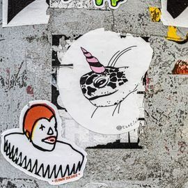 Stickers on a gray surface: clown, lizard with pink unicorn horn, and geometric shapes.