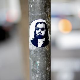 Sticker of a man with sunglasses, beard, and long hair on a pole.