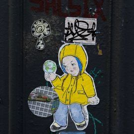 Child in yellow raincoat holding magnifying glass; urban wall with stickers.