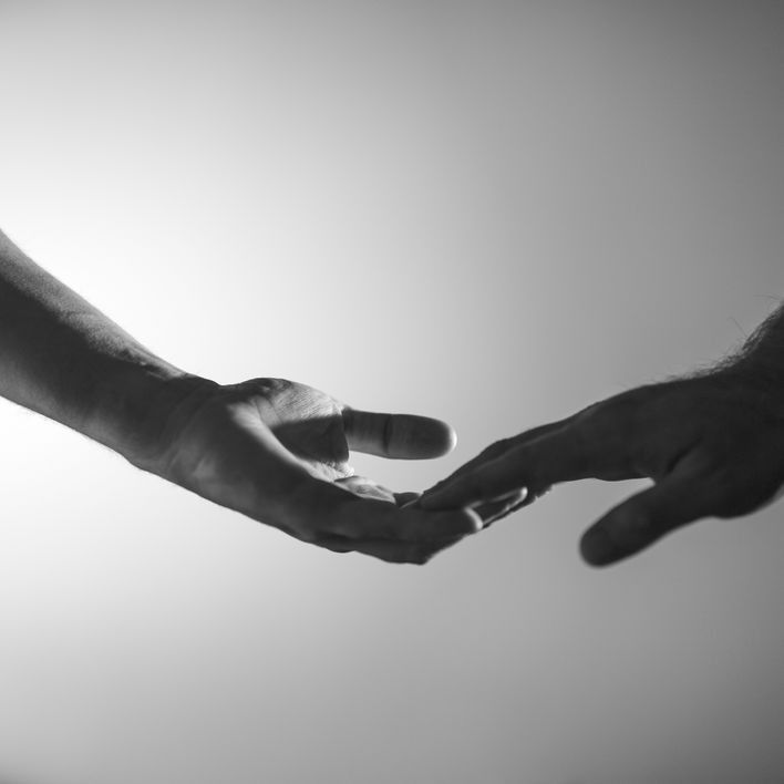 Two hands reaching toward each other in black and white. Fingers almost touching.