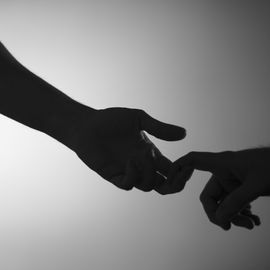 Silhouetted hands reaching toward each other, one hand nearly touching the other.