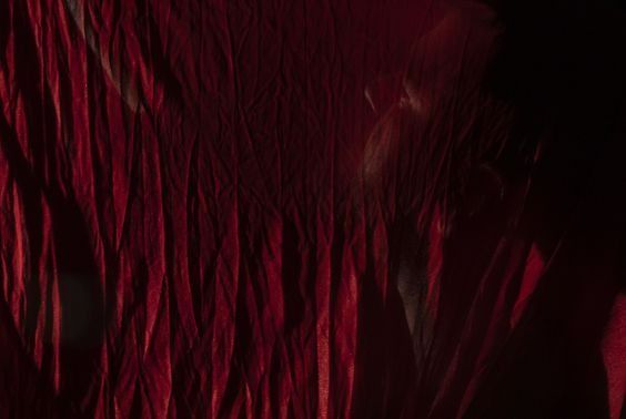 Red fabric waves with a blurred, obscured figure partially visible in shadows.