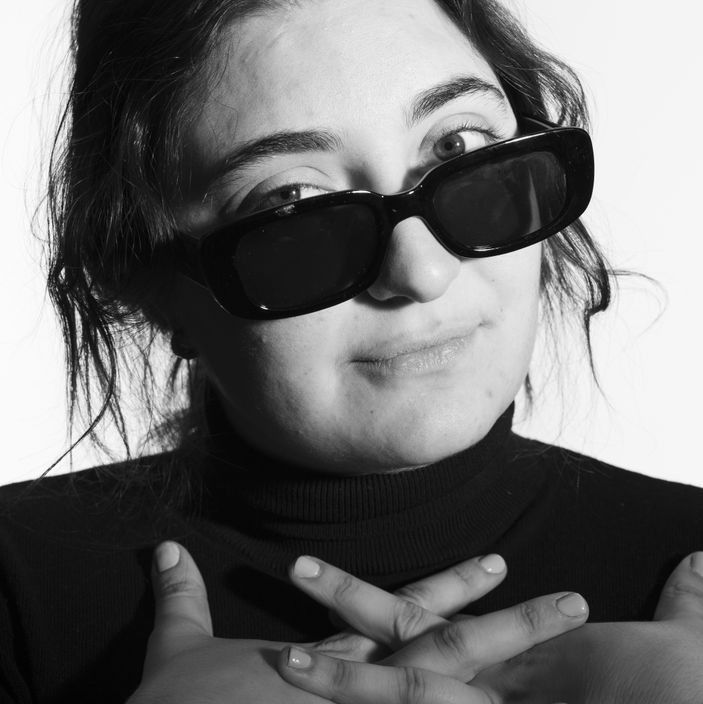 Person wearing black sunglasses and turtleneck, hands crossed over chest, looking up.