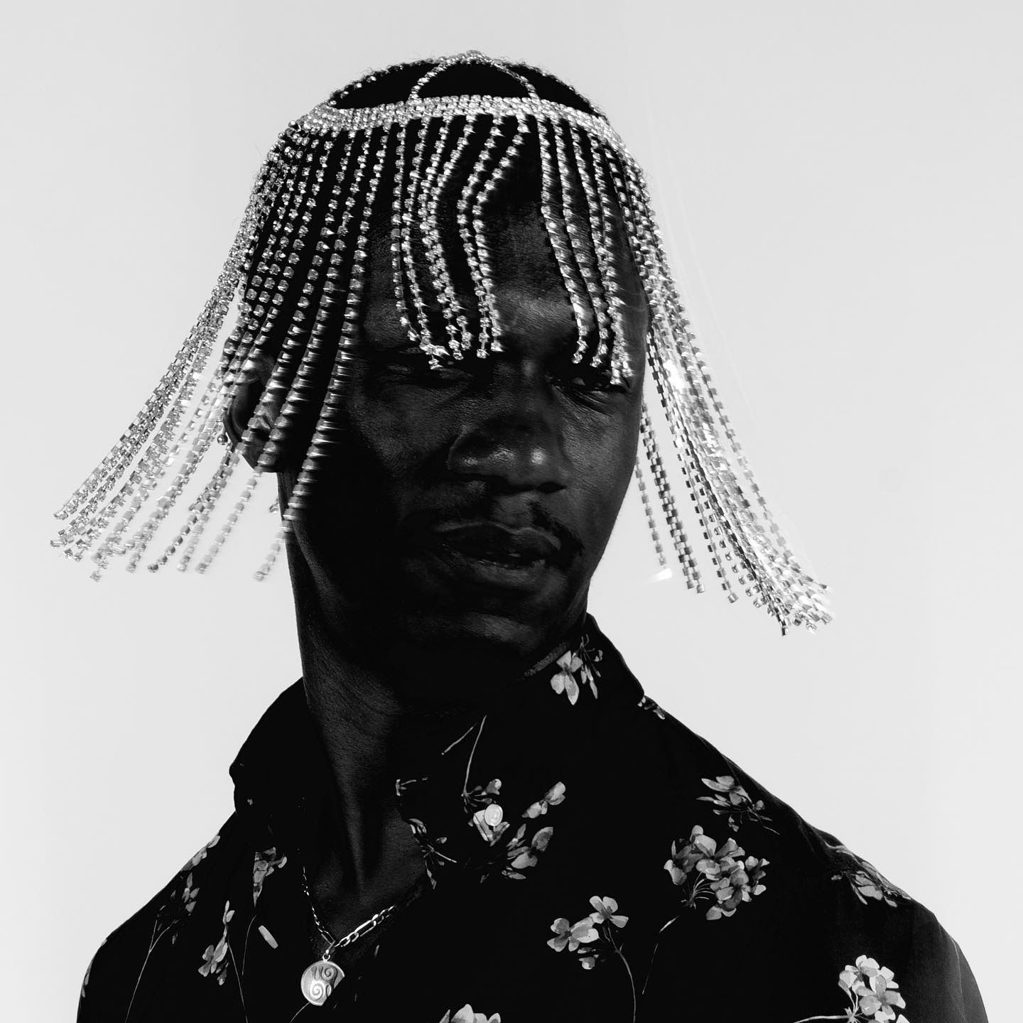 Black and white portrait of a person wearing a jeweled headpiece with fringe, floral shirt.
