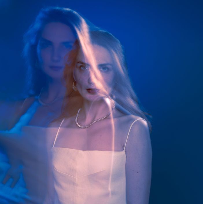 Woman in a white dress, blurred double exposure. Blue background, necklace, and intense gaze.
