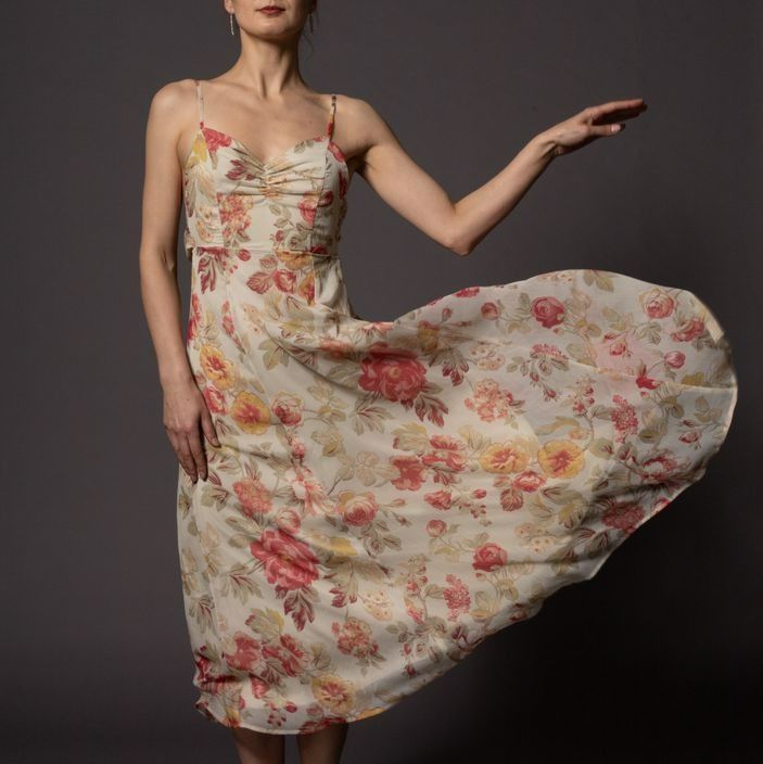 Woman in a floral sundress, arm outstretched, dress billowing, against a gray backdrop.