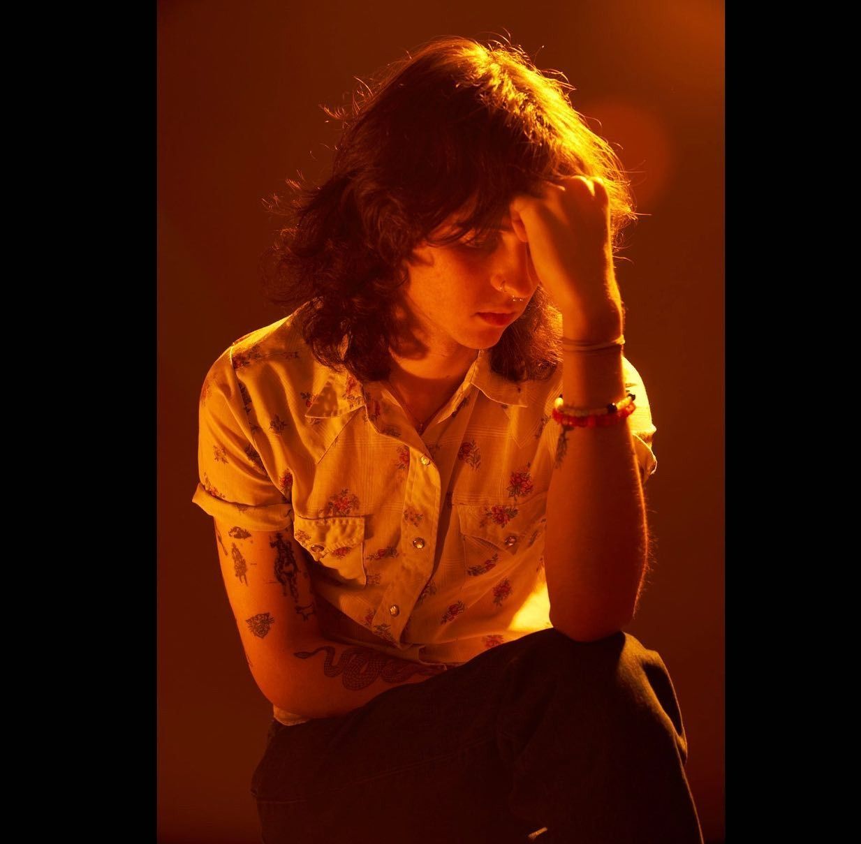 Person with hand on head, seated, lit by warm light.