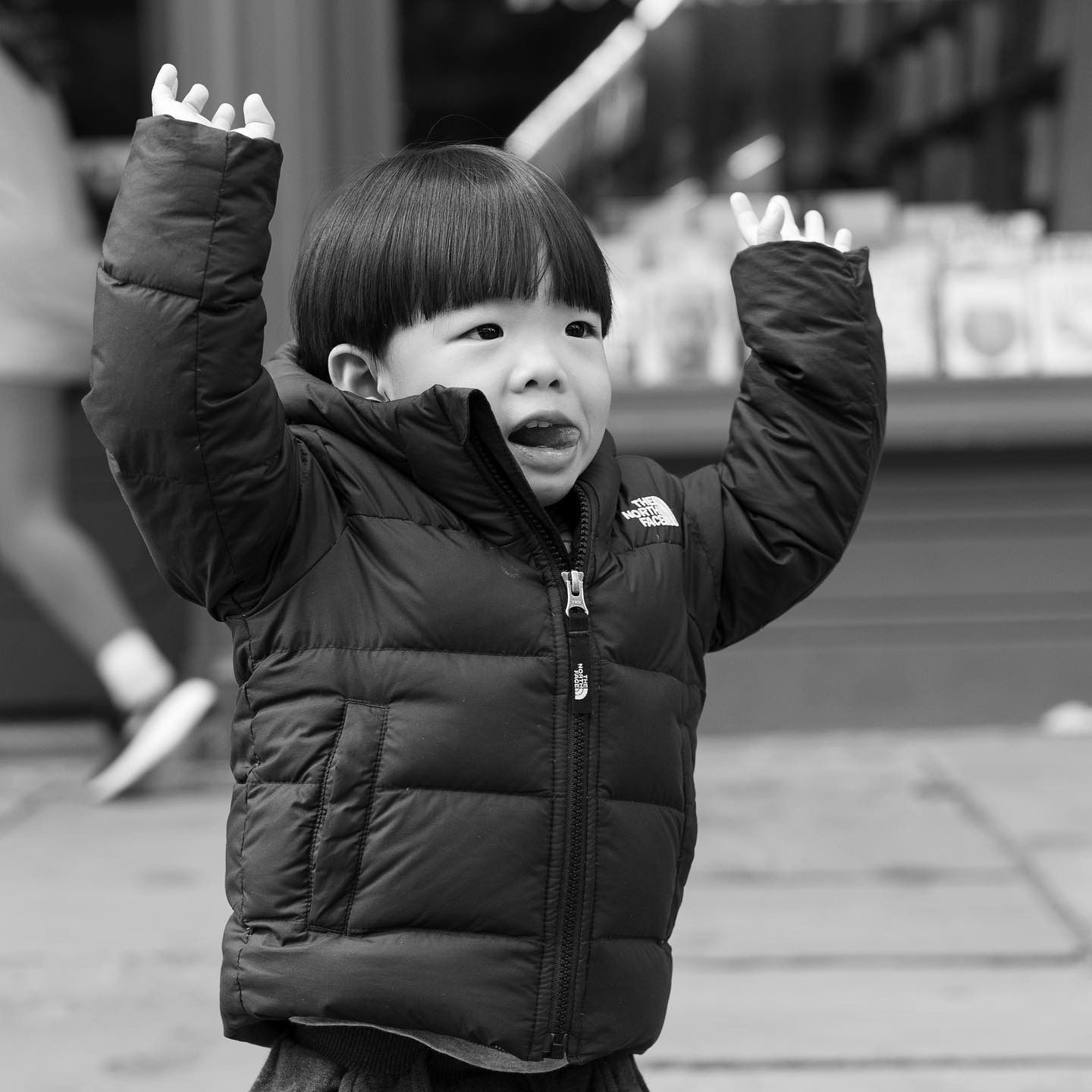 Child in black puffer jacket, arms raised, mouth open, likely expressing joy or excitement.