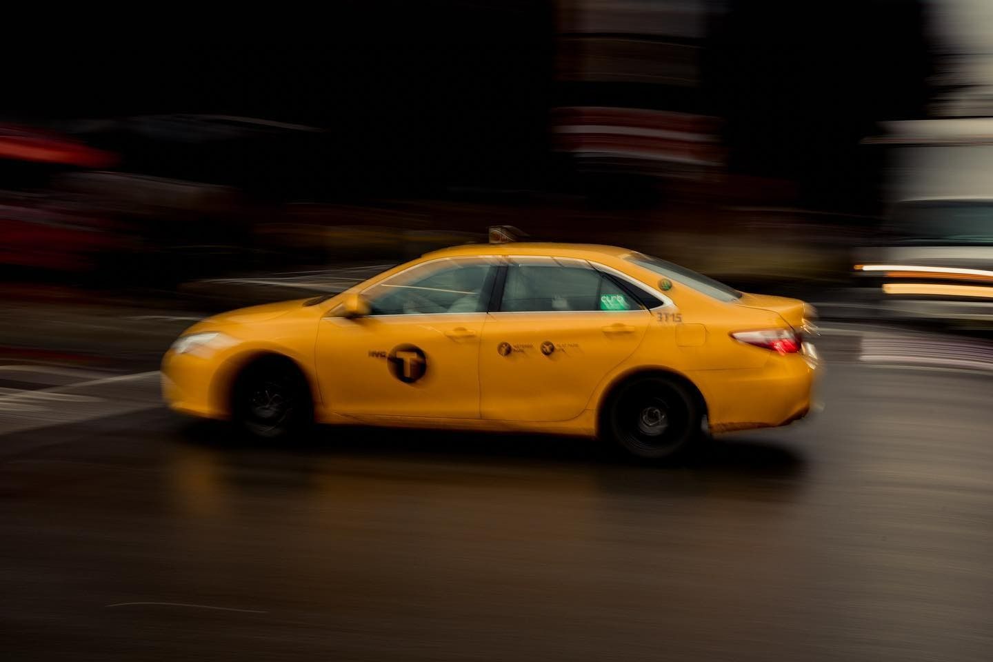 Yellow taxi cab speeding on wet street, blurring lights in background.