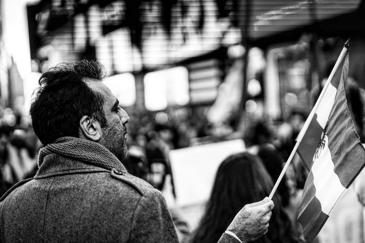 Man holding flag in protest, looking upward. Crowd in the blurred background.