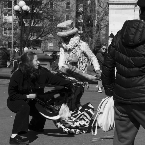 A street performer with a top hat dances with a person in a public space. A person stands nearby.