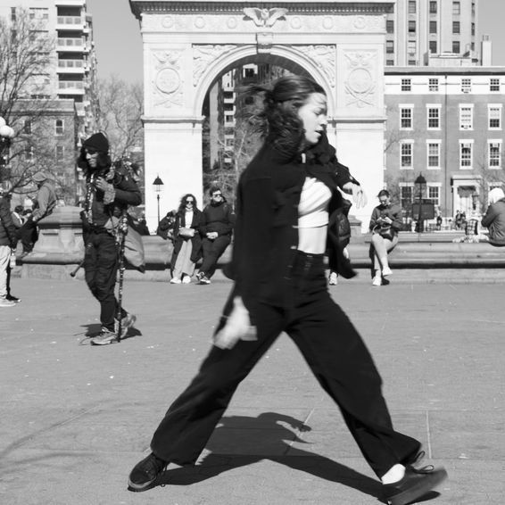 Woman walking in Washington Square Park, New York City, near iconic arch; black and white.