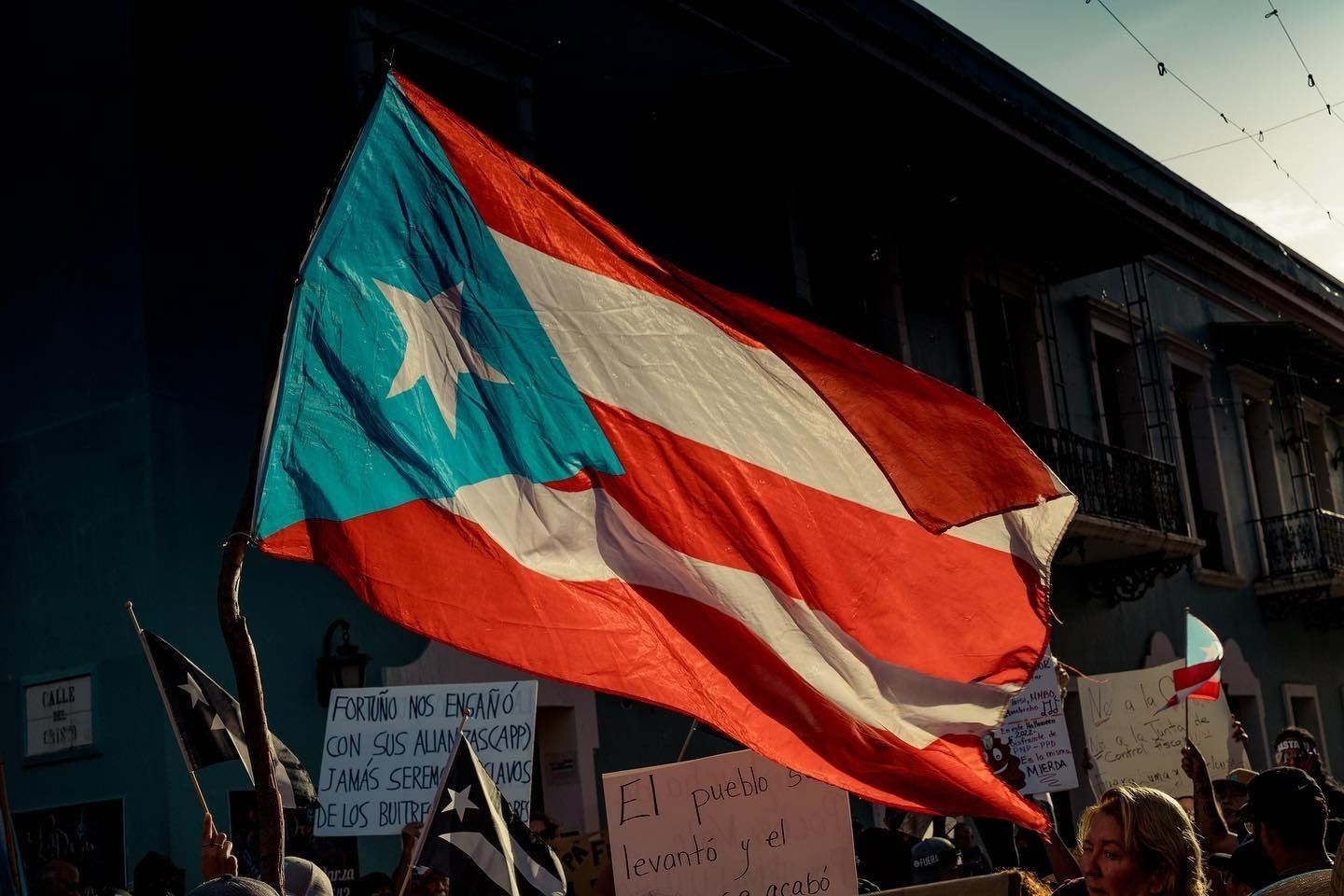 Puerto Rican flag waving over a crowd of people and buildings; red, white, and blue colors.