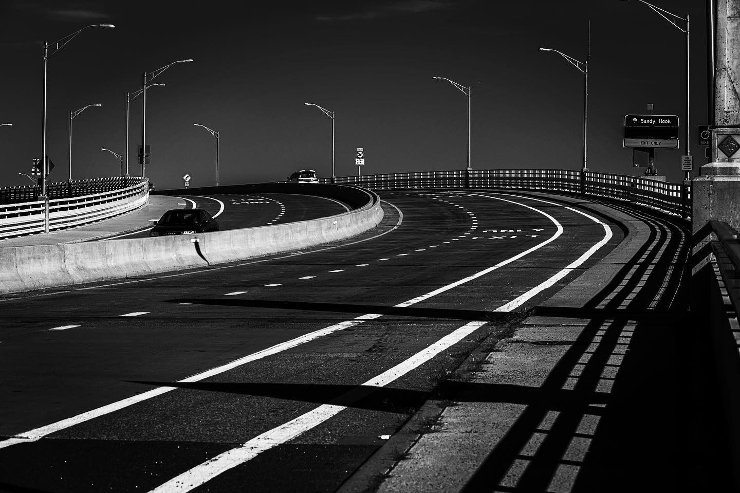 Black and white photograph of a curved bridge road with street lights and a concrete barrier.