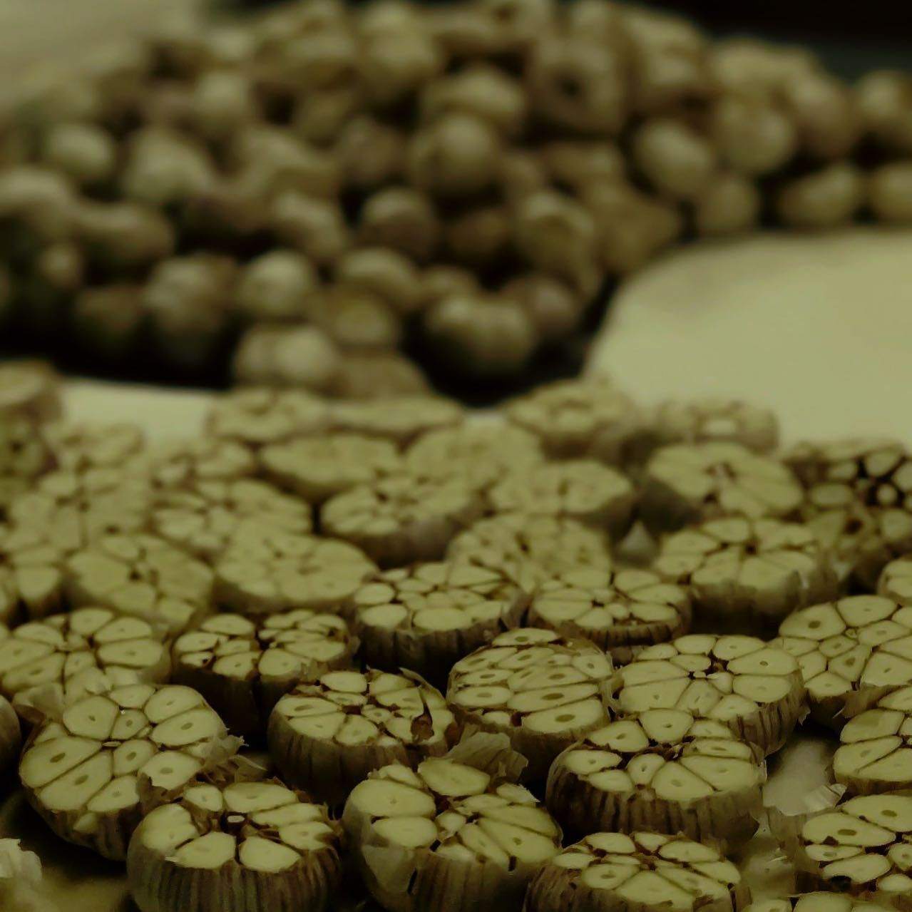Sliced garlic bulbs, cut side up, arranged on a surface with a larger pile of whole bulbs in the background.