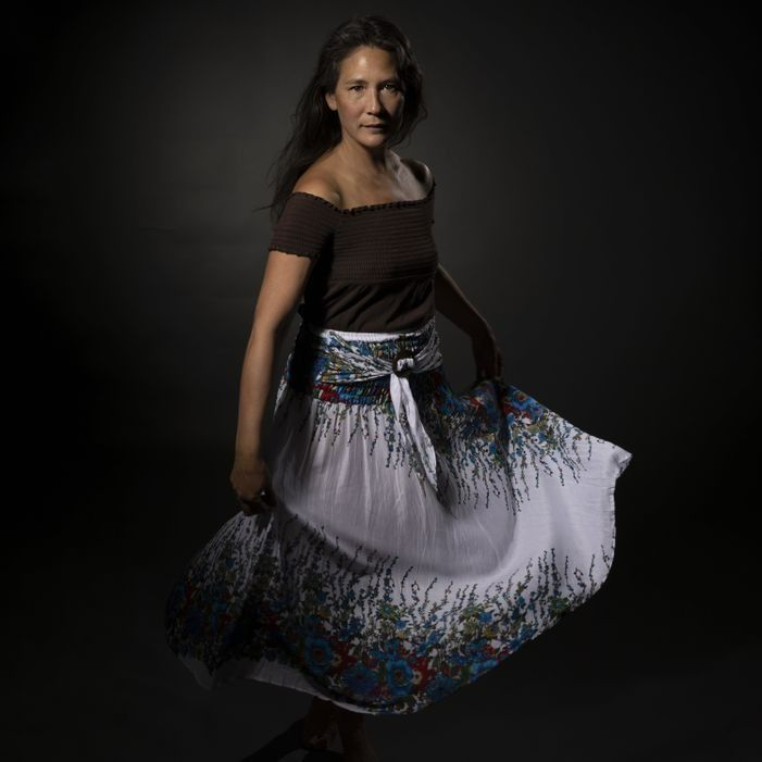 Woman in brown top and patterned skirt twirling against a dark background.