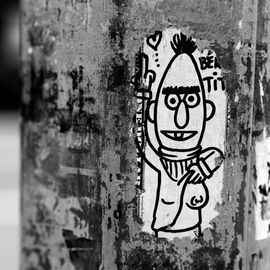 Black and white street art sticker of a cartoon character with a paintbrush, on a textured pole.