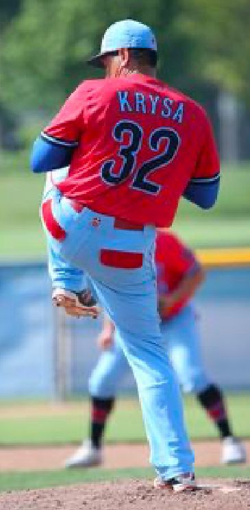 A person wearing a hat and orange shirt, holding a baseball bat on their shoulder on a baseball field.