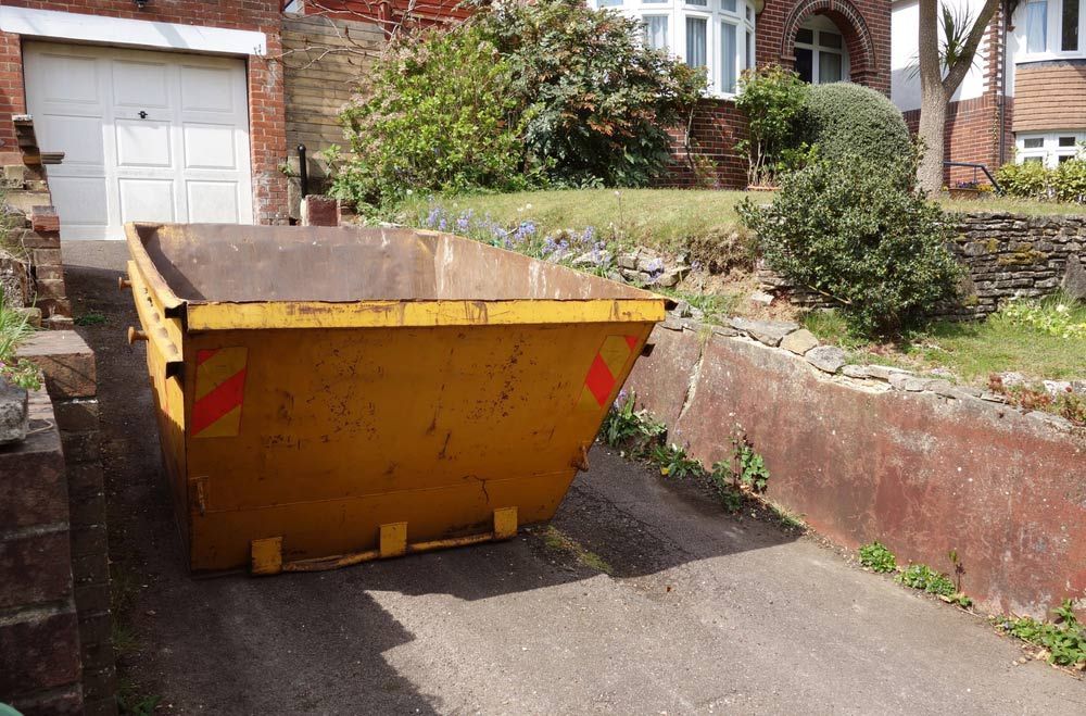 A Yellow Dumpster is Parked in a Driveway in Front of a House — Grafton Skip Hire–Zims Bins in Coffs Iluka, NSW
