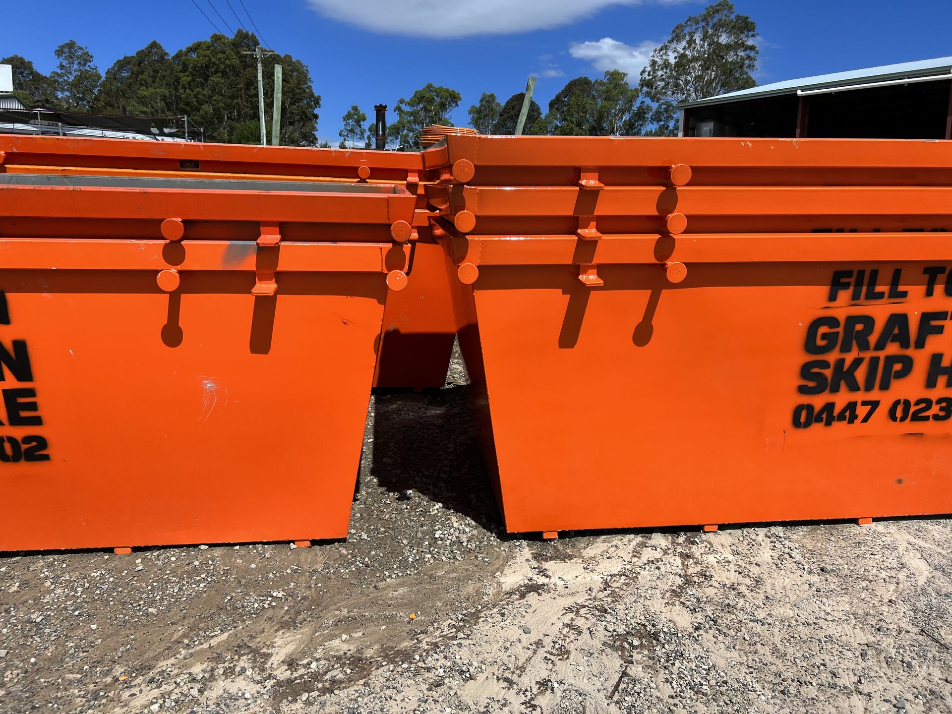 A Yellow Dumpster is Sitting in the Grass Next to Some Wooden Pallets — Grafton Skip Hire–Zims Bins in Maclean, NSW