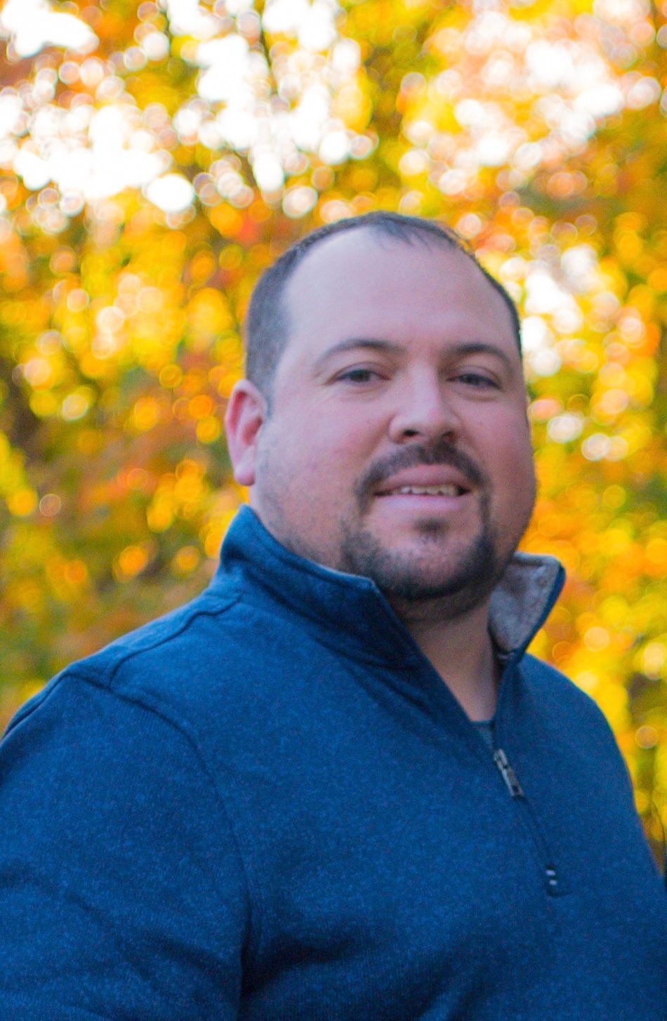 A man with a beard is wearing a blue sweater and smiling.