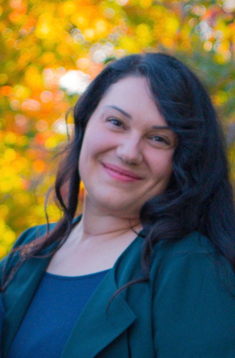 A woman in a green jacket and blue shirt is smiling for the camera.