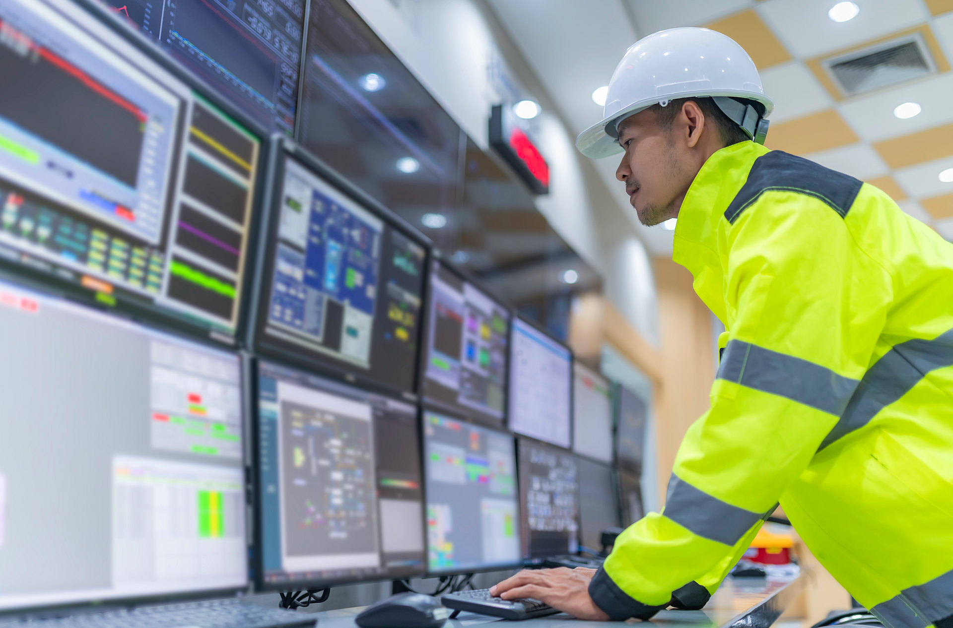 A man in a hard hat is working on a computer in a control room.