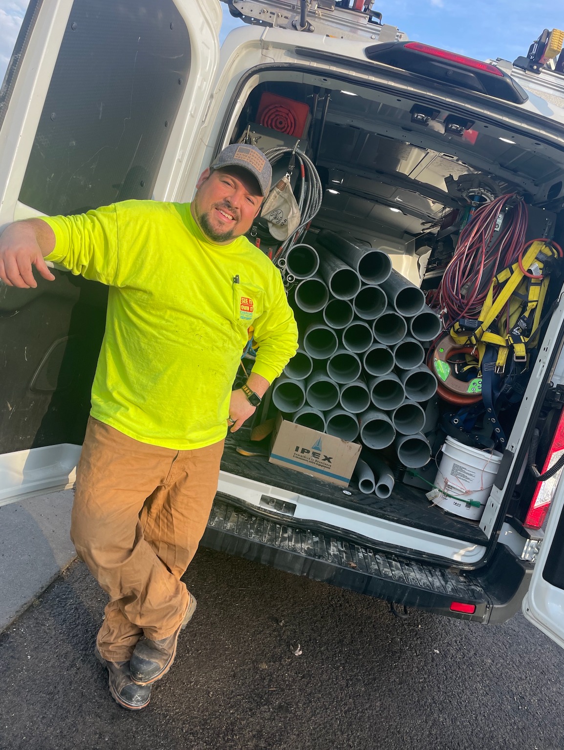 A man in a neon yellow shirt is standing in front of a van filled with pipes.