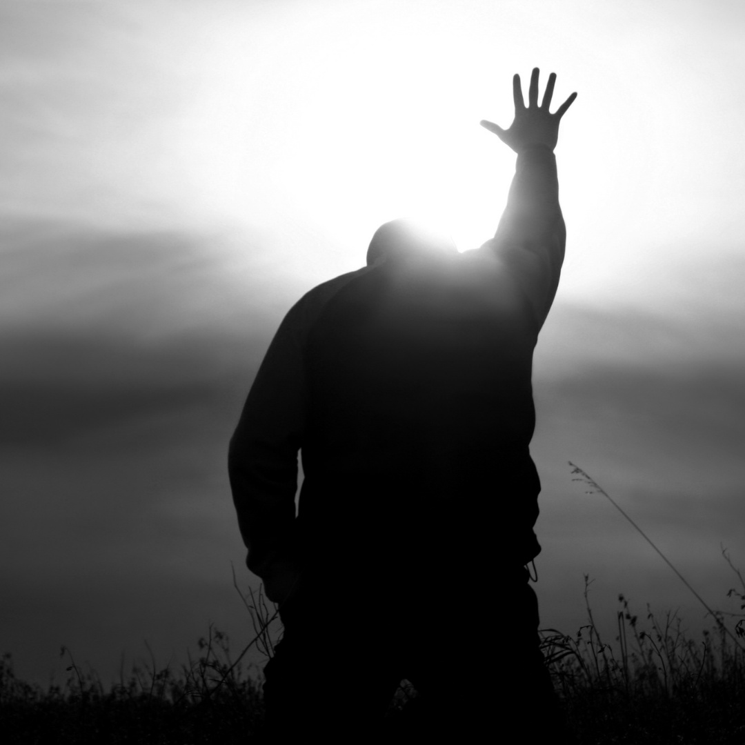 Silhouette of a person with arm raised, hand open towards bright sun.