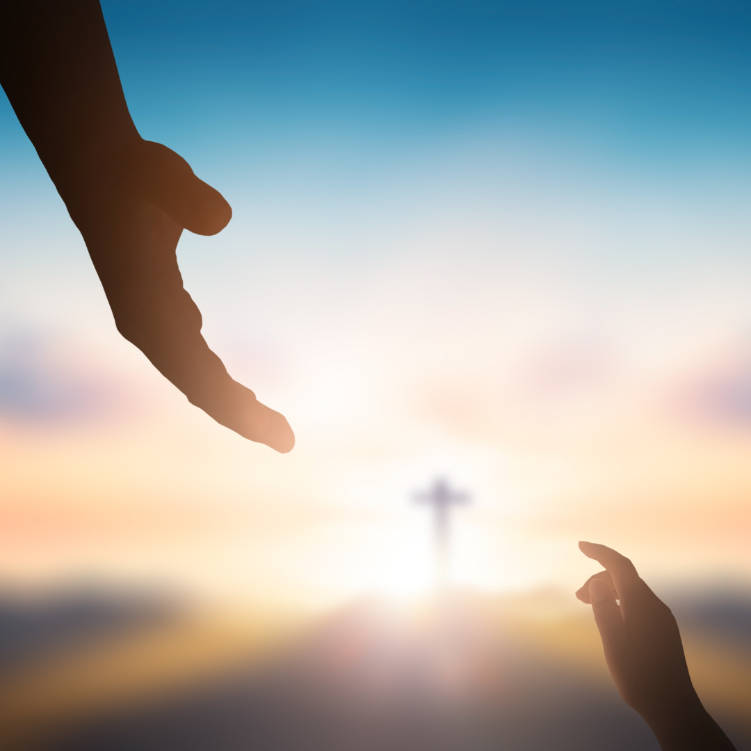 Silhouetted hands reaching toward each other with a blurred background of a cross and sunset.