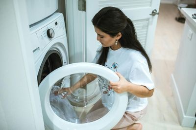 A woman is putting clothes in a washing machine.