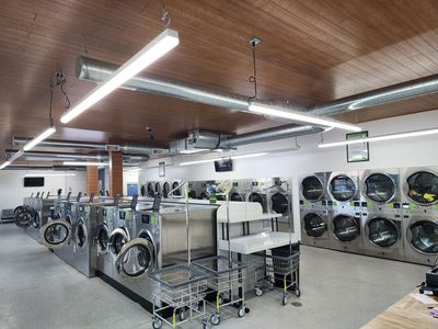 A row of washing machines in a laundromat filled with clothes.