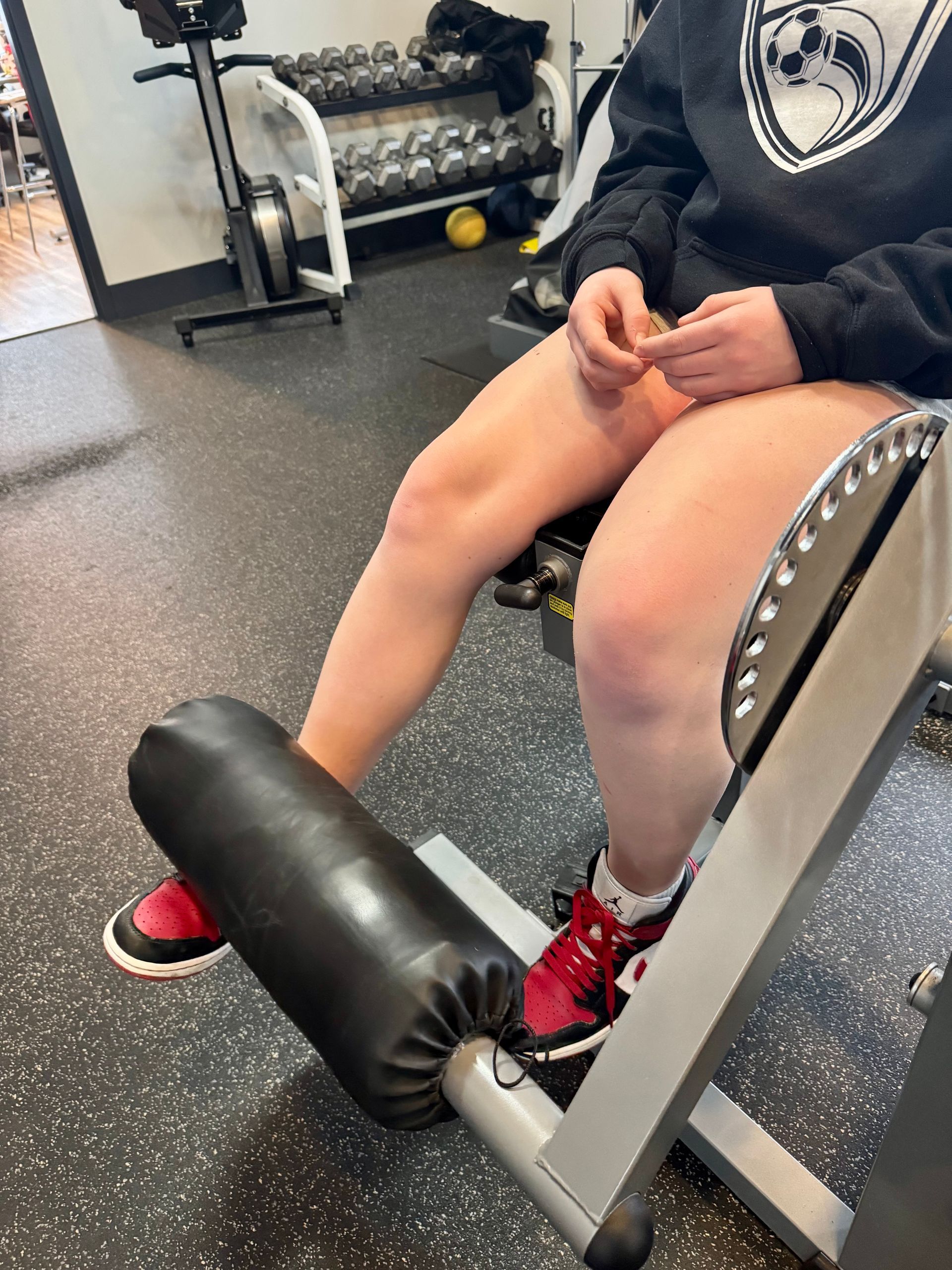 A person is sitting on a leg extension machine in a gym.