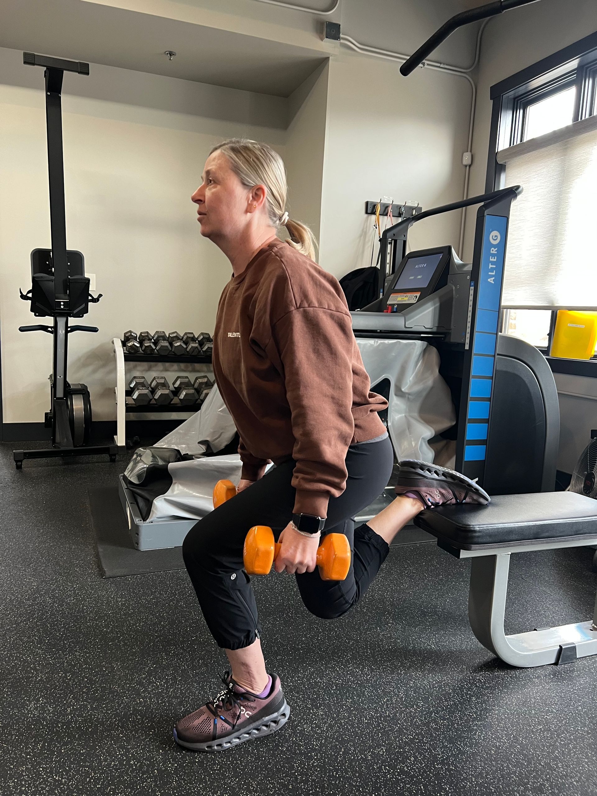 A woman is doing squats with dumbbells in a gym.