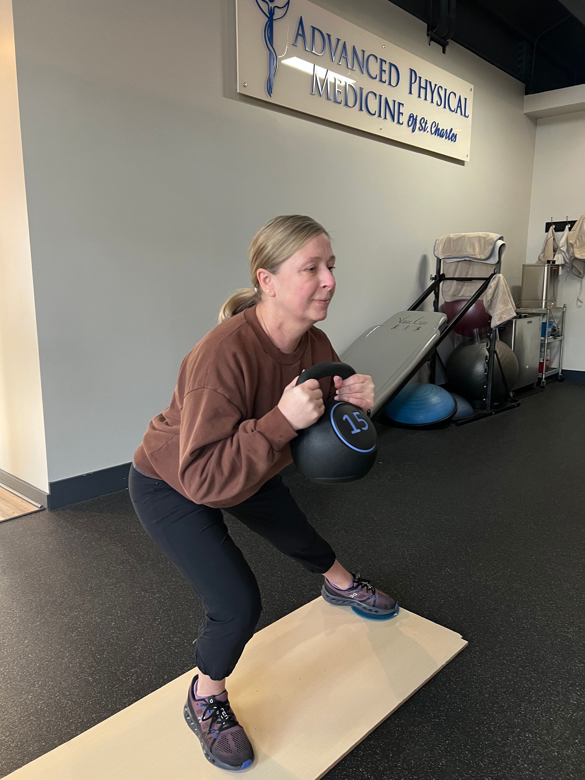 A woman is squatting with a kettlebell in a gym.