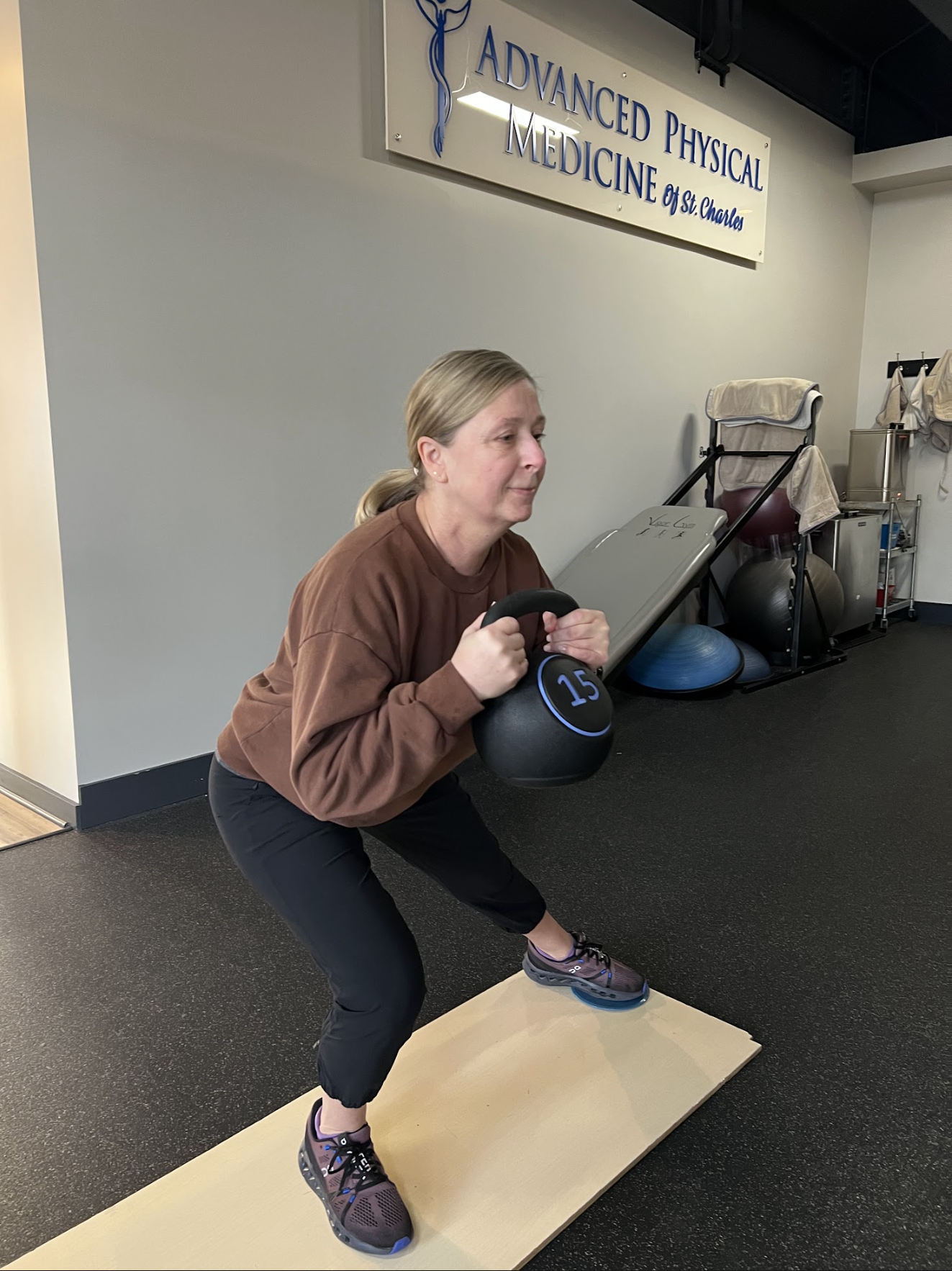A person performing a kettlebell goblet squat on a mat in a physical medicine clinic.