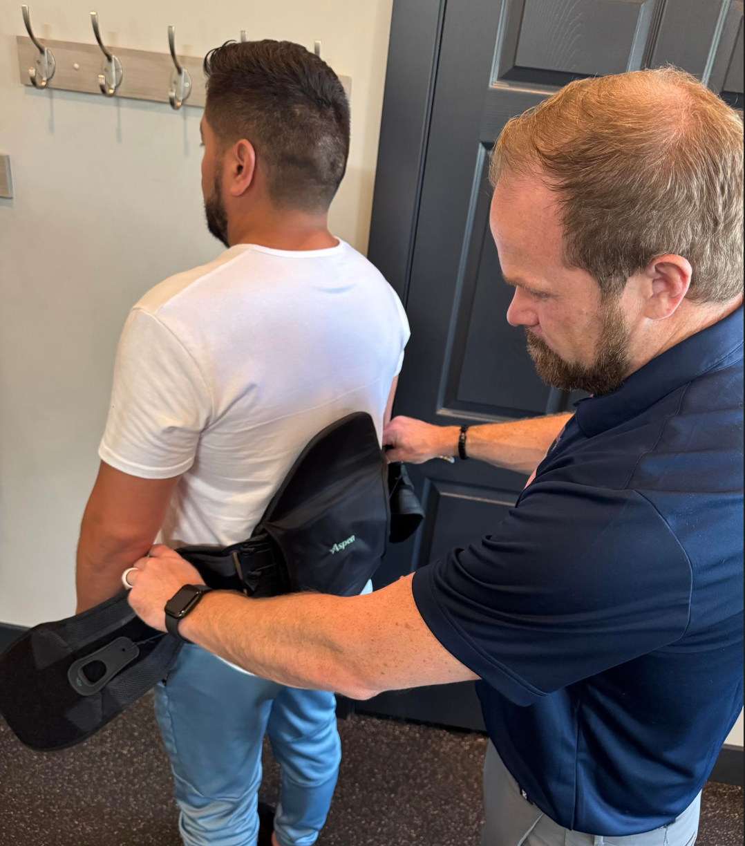 A clinician adjusts a black lumbar support brace on a person's lower back in a professional office setting.