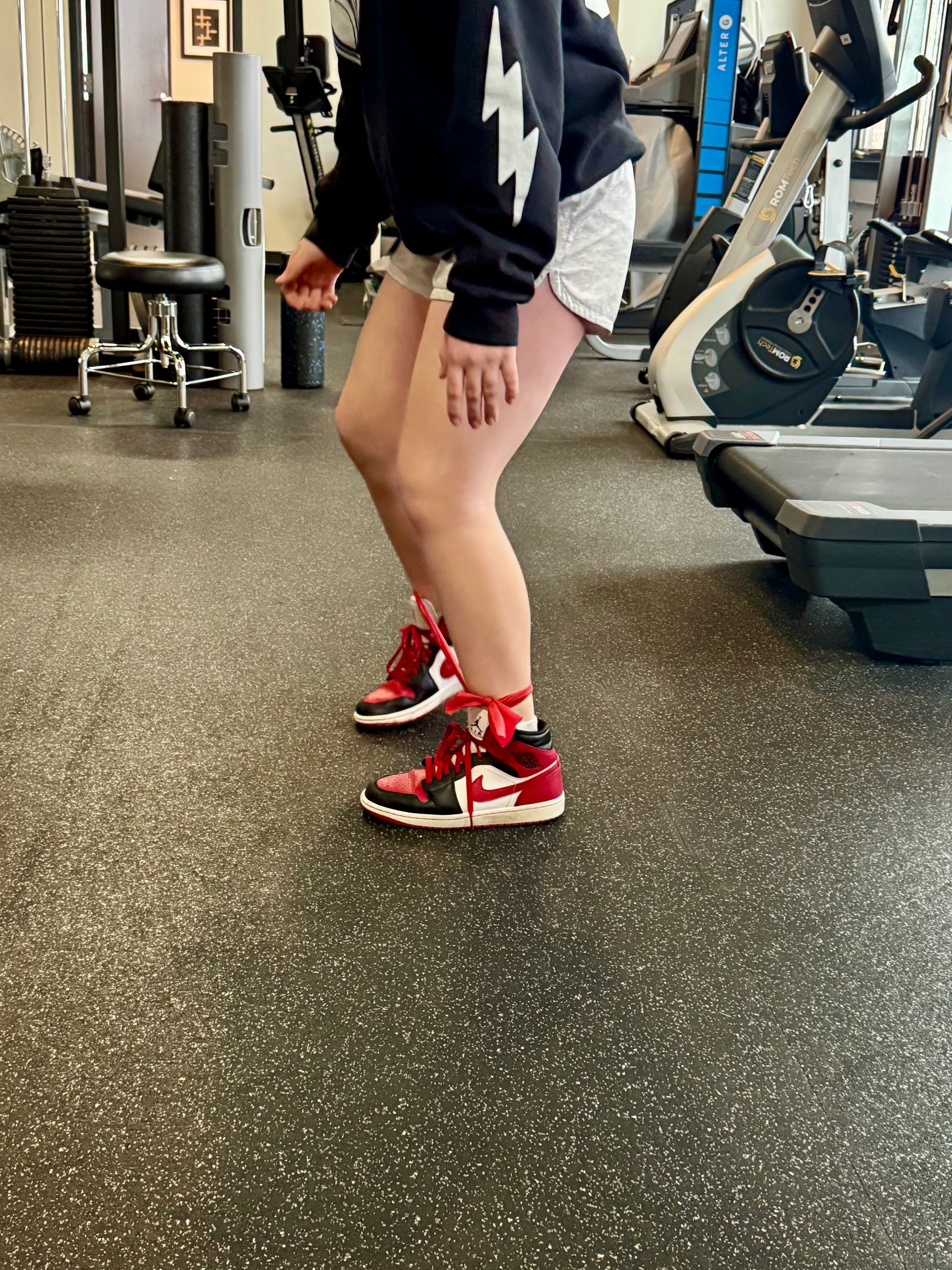 A person wearing red and black sneakers is jumping in a gym.