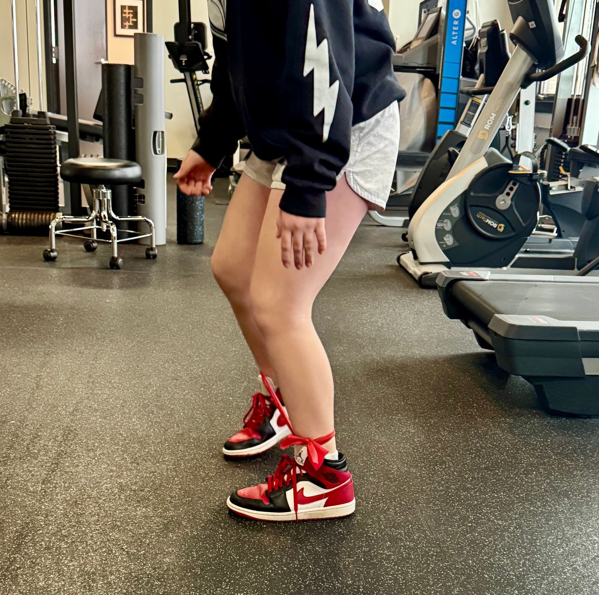 A person wearing red and black sneakers is jumping in a gym.