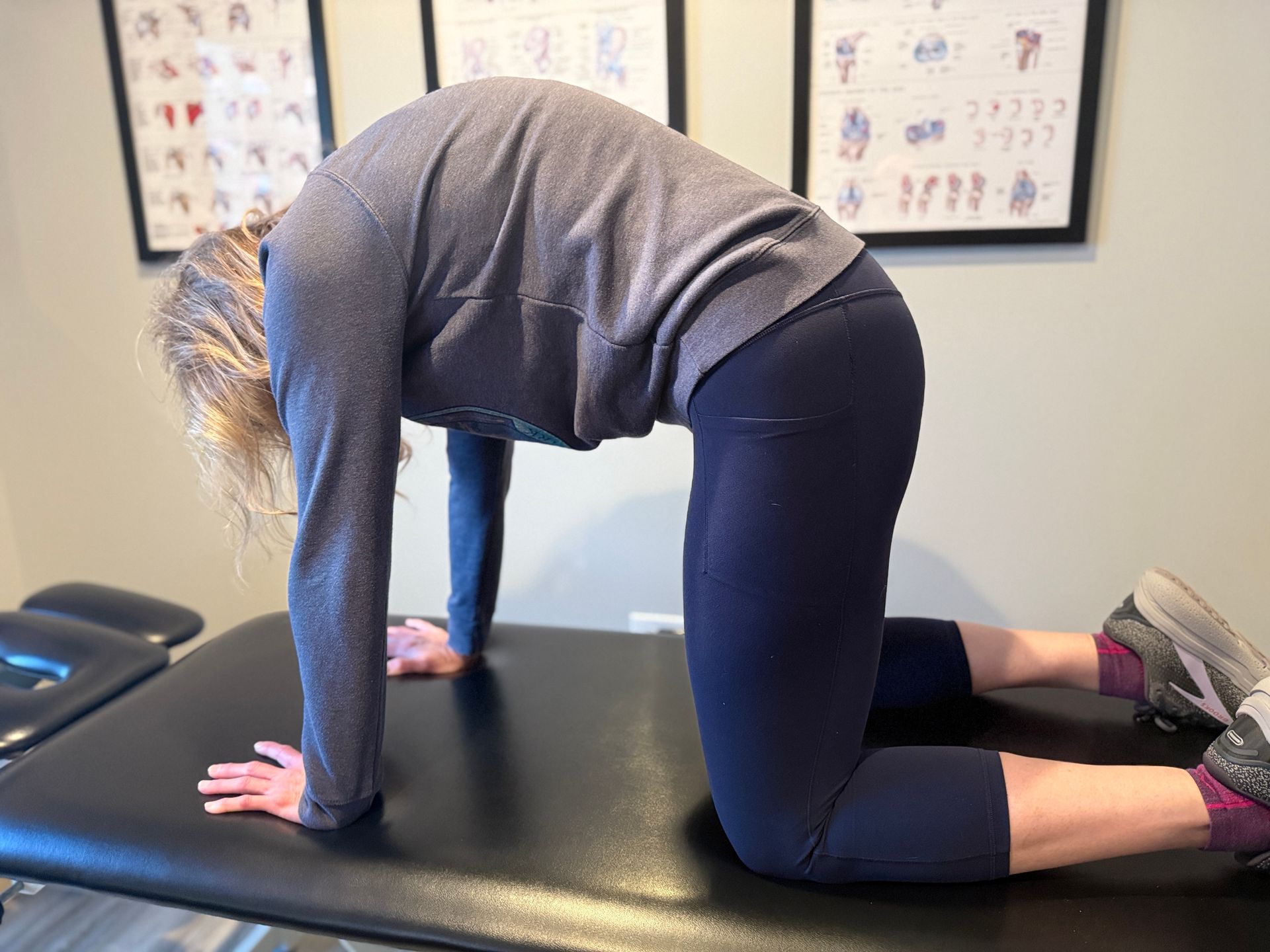 Person performing a cat stretch on a black table; hands and knees on the table, back arched.