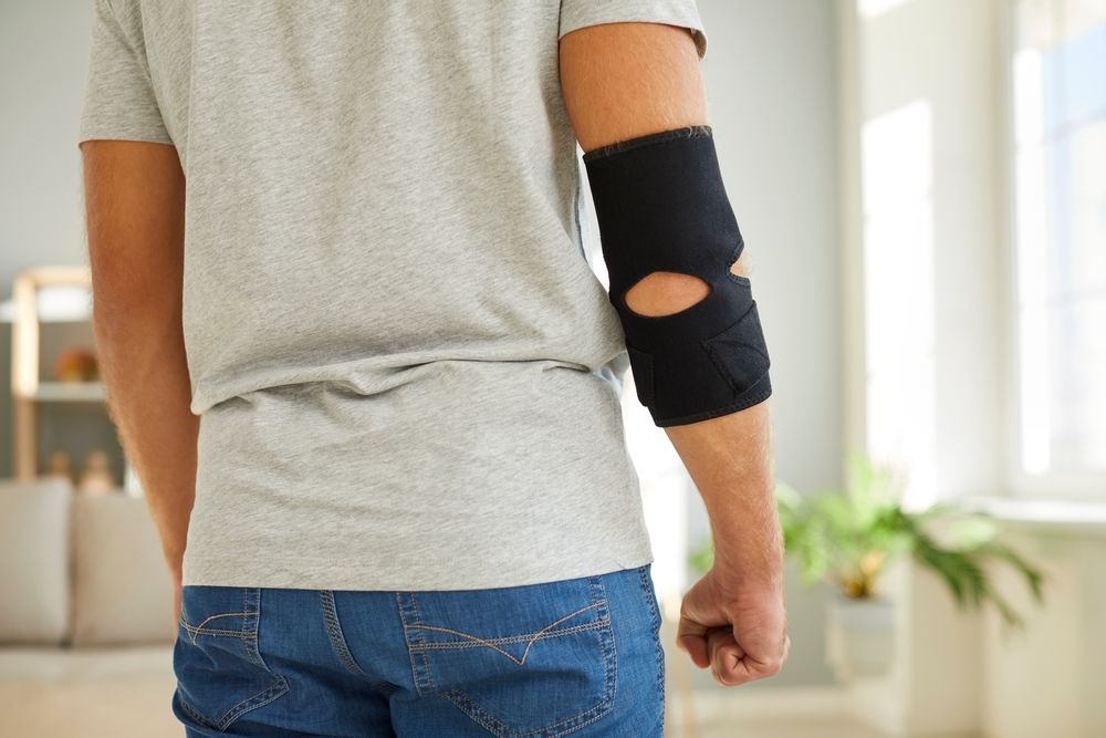 A man wearing an elbow brace is standing in a living room.