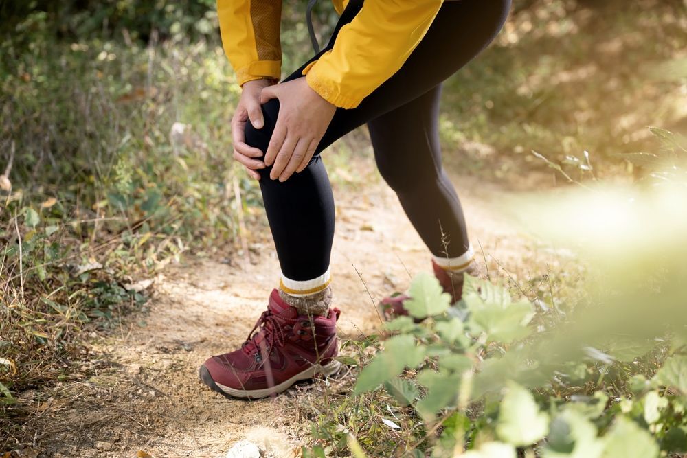 A woman holding her knee while hiking due to pain.