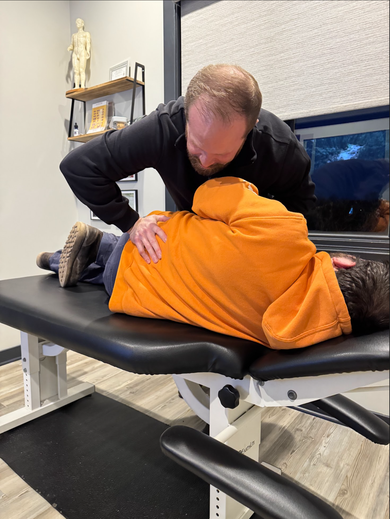 Chiropractor adjusting a patient's back on an examination table. The patient is lying facedown.