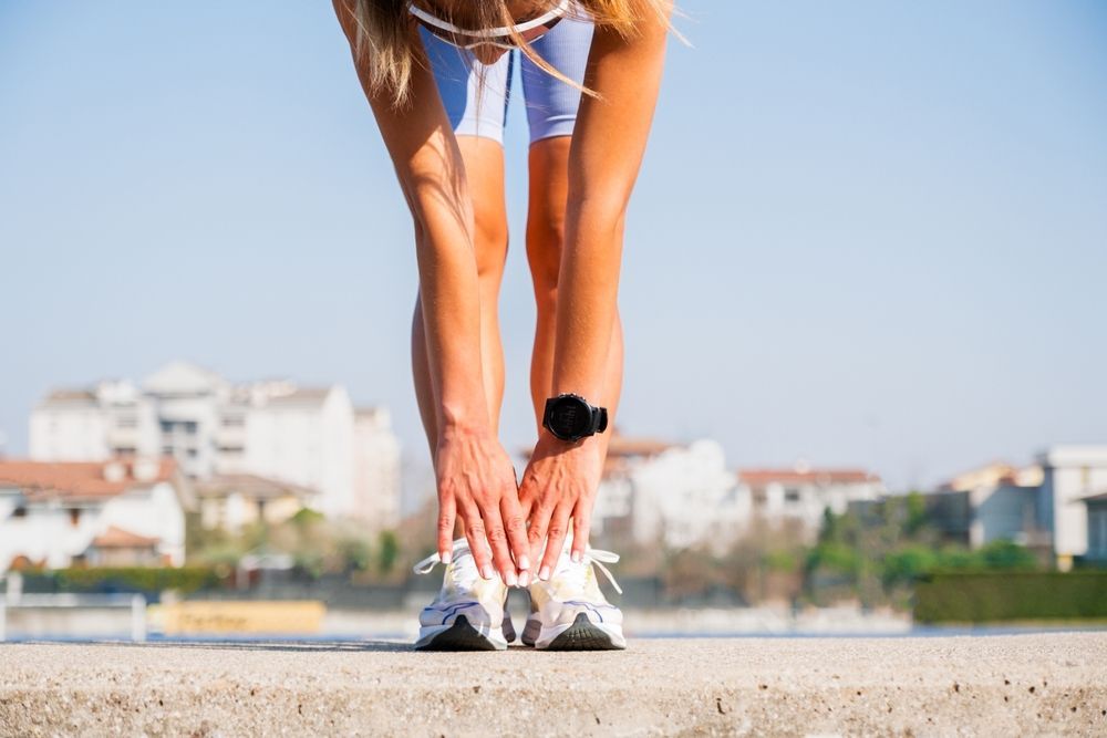 Woman stretching legs, touching toes, wearing athletic wear outdoors.