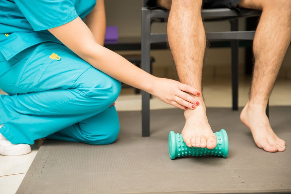 a nurse is kneeling down to massage a patient 's foot with plantar fasciitis.