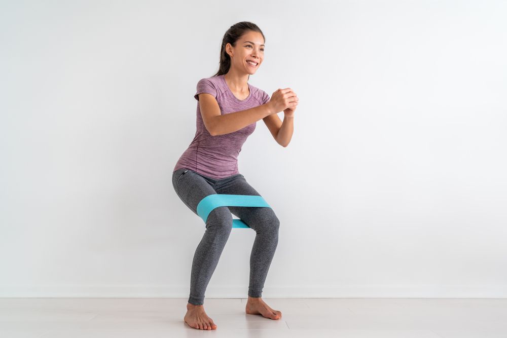 A woman is squatting with a resistance band around her knee.