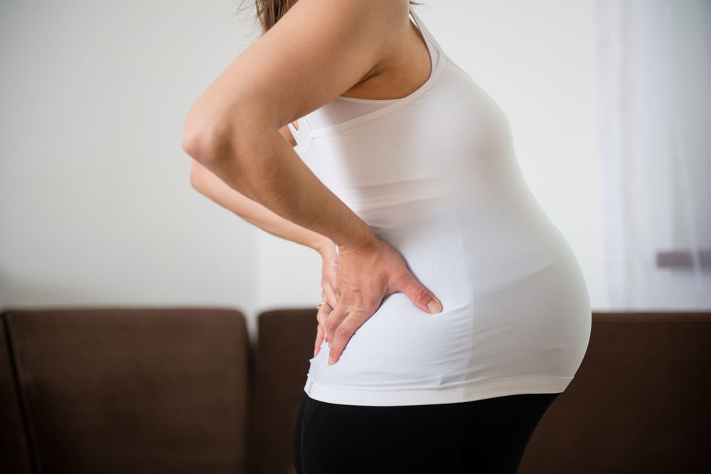 A pregnant woman is holding her back in pain.