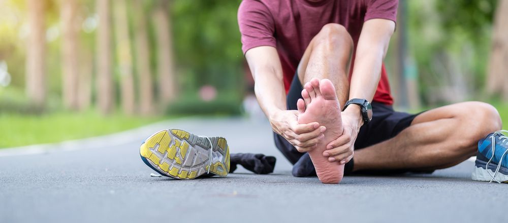 runner sitting on ground rubbing foot with plantar fasciitis.