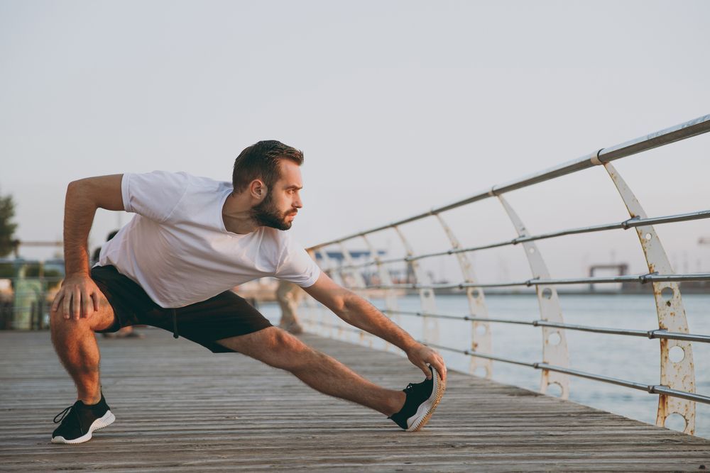 A man is stretching his legs on a pier.