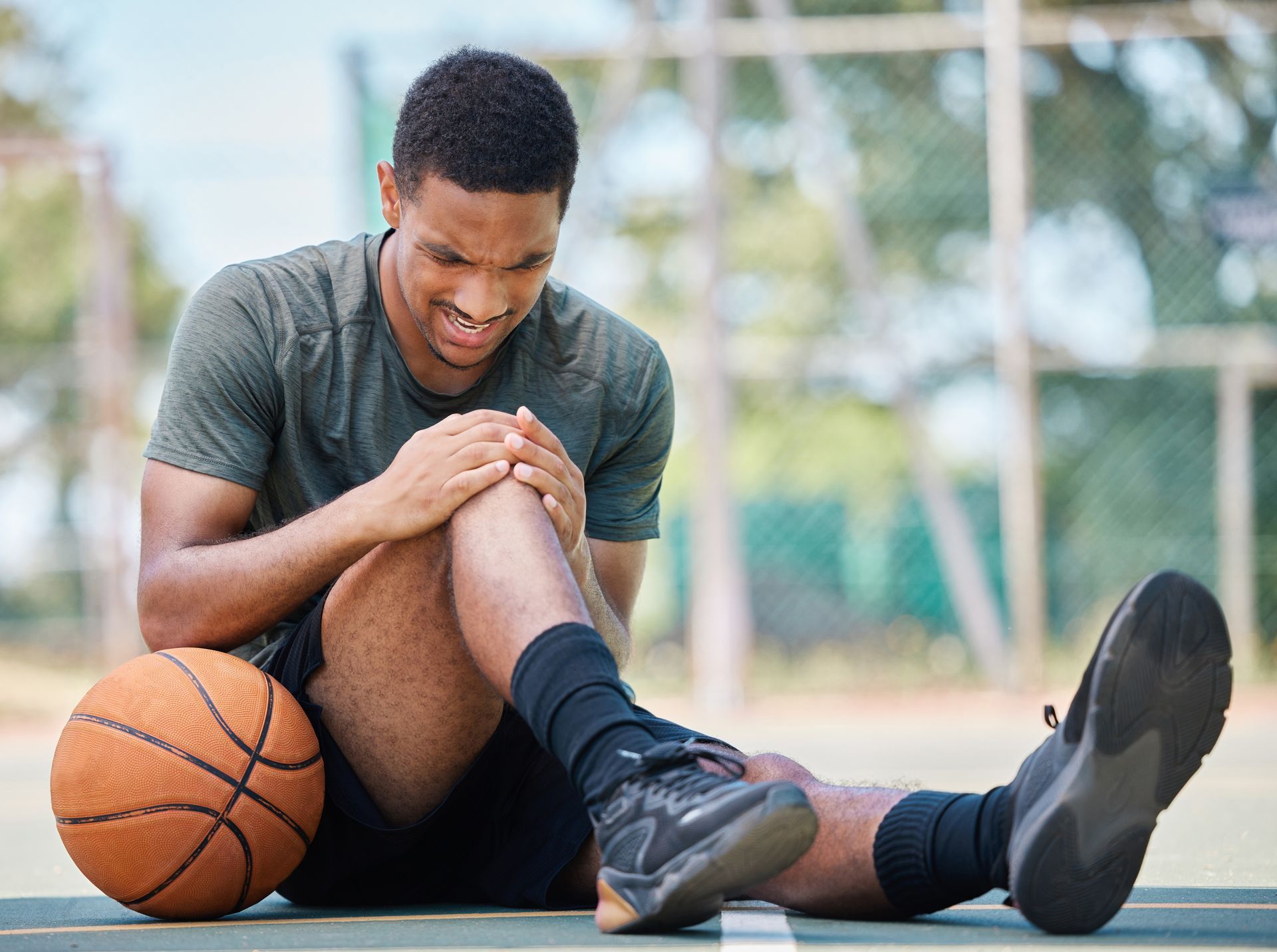 a man is sitting on the ground with a basketball and holding his knee after an ACL injury